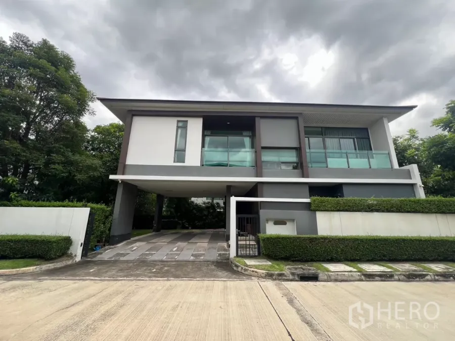 独立式住宅 出租在Bang Kapi, Bangkok - 现代两层转角别墅，玻璃阳台与车棚，绿篱环绕。