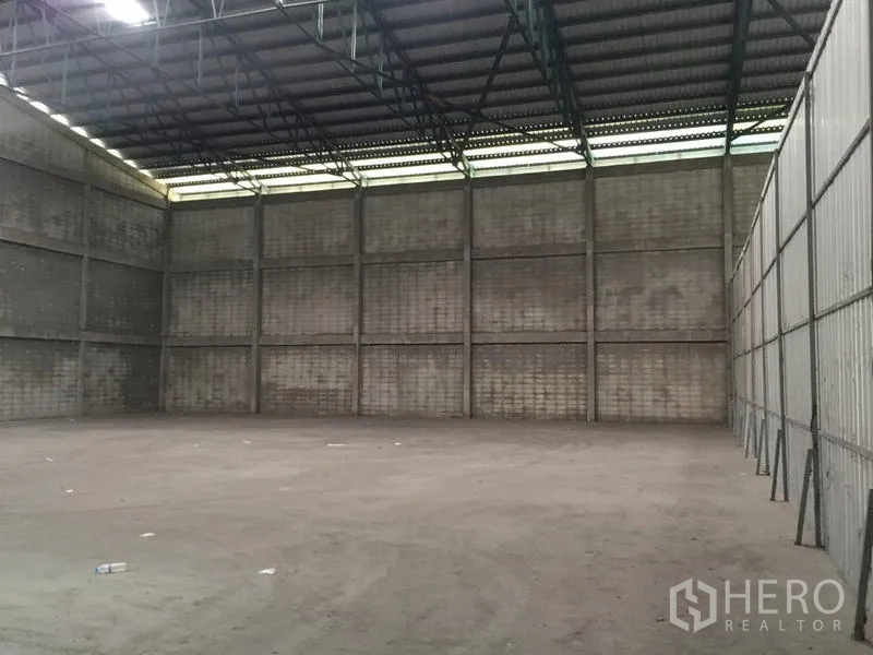 Warehouse for rent in Mueang Pathum Thani, Pathum Thani - Empty high-bay warehouse space with ventilated roof panels and block walls ready for storage.