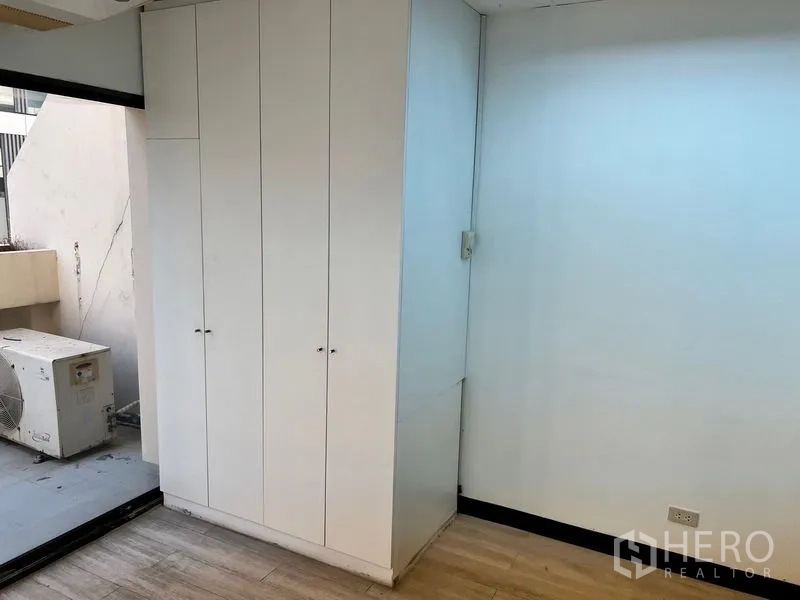 办公空间 出租在Pathum Wan, Bangkok - 内置白色储物柜，旁边是通往小阳台的推拉门，室外机可见。
