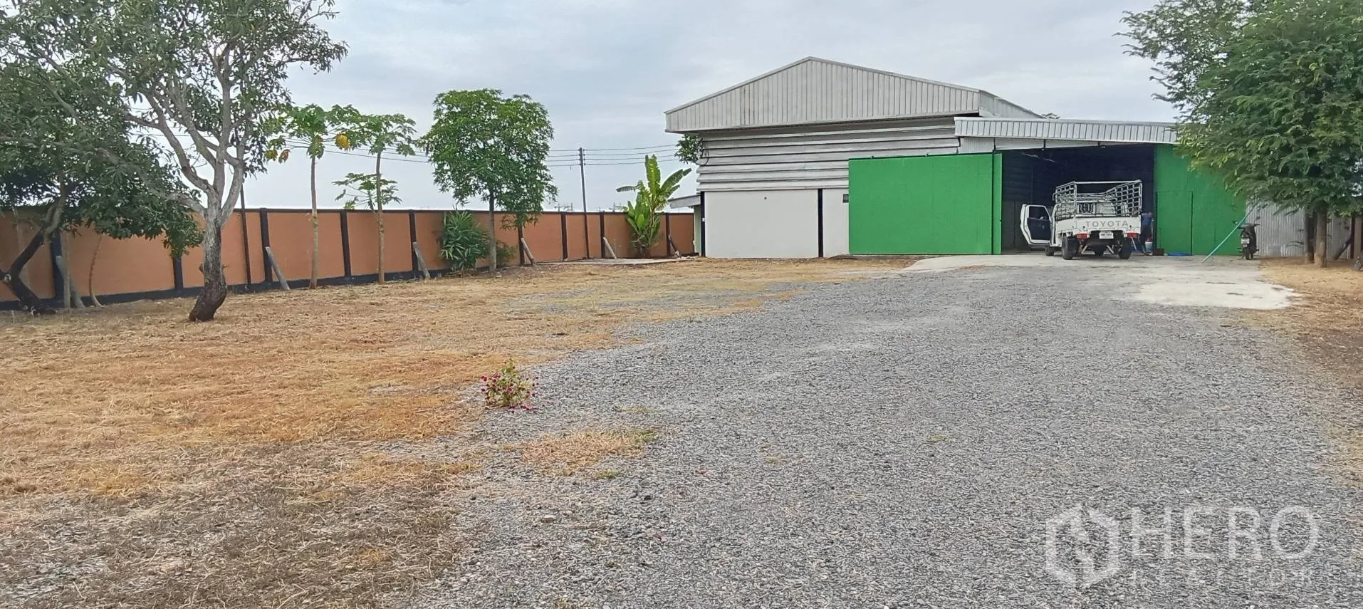 Warehouse for sale in Lam Luk Ka, Pathum Thani - Gated warehouse compound with gravel driveway, large yard and loading access.