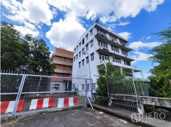 工厂 出租在Phra Samut Chedi, Samut Prakan - 带大门入口的独立工业园区，旁有多层办公楼和蓝天白云。