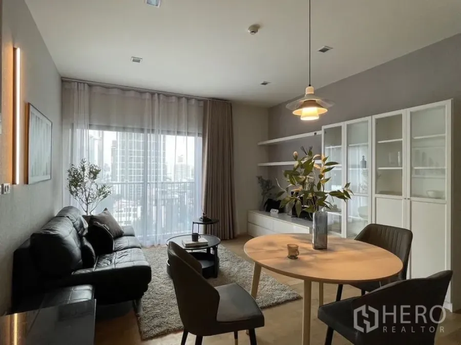 คอนโด ให้เช่าในWatthana, Bangkok - พื้นที่นั่งเล่นและรับประทานอาหารแบบเปิด มีโซฟาหนังสีดำ โต๊ะกลม และหน้าต่างสูงจรดเพดานเห็นวิวเมือง