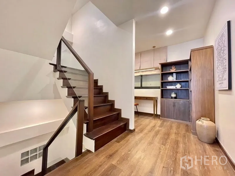 Townhouse for rent - Stair landing with glass railing, shelving, and warm decor.