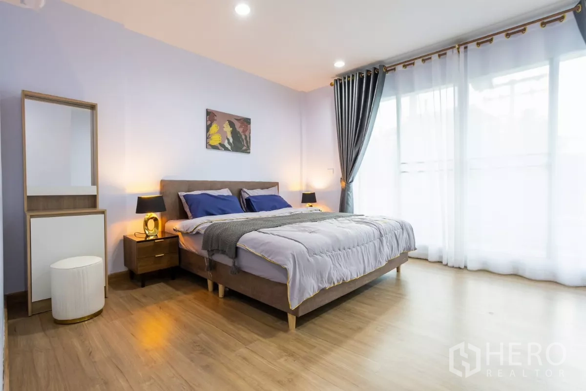 ทาวน์เฮาส์ ให้เช่า - ห้องนอนใหญ่ พื้นไม้ เตียงคิงไซซ์ และผ้าม่านสองชั้นเปิดสู่ระเบียง