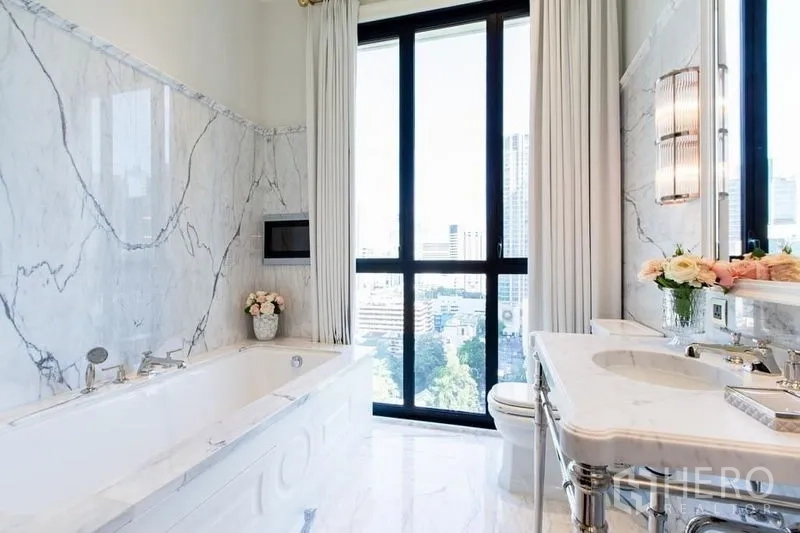 Condominium for sale in Pathum Wan, Bangkok - Luxurious marble bathroom with soaking tub and floor-to-ceiling window overlooking Bangkok.