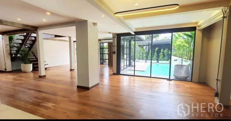 Home Office for rent or sale in Khlong Toei, Bangkok - Large living area with wooden floors and sliding doors opening to the pool terrace.