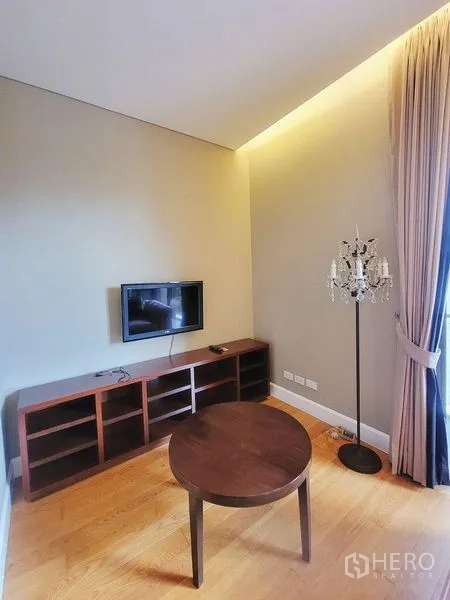คอนโด ให้เช่าในWatthana, Bangkok - มุมทีวีอบอุ่น ทีวีติดผนัง ชั้นวางไม้ โต๊ะกาแฟทรงกลม และผ้าม่านสูง