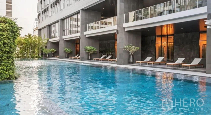 Condominium for sale in Pathum Wan, Bangkok - Outdoor lap pool with sun loungers beside a contemporary condominium façade and greenery.