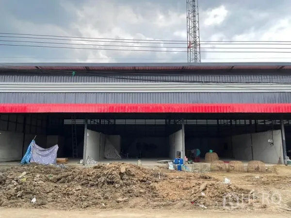 货栈 出租在Pathum Thani - 红灰金属板外立面的仓库，正面开口宽阔，前方为施工土地。