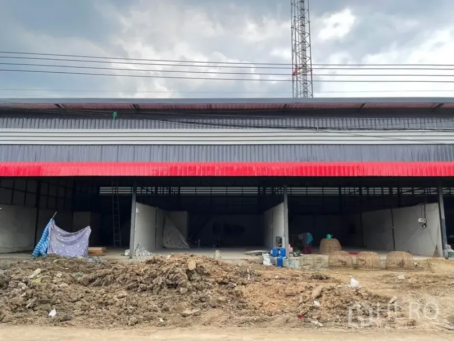 货栈 出租在Pathum Thani - 红灰金属板外立面的仓库，正面开口宽阔，前方为施工土地。