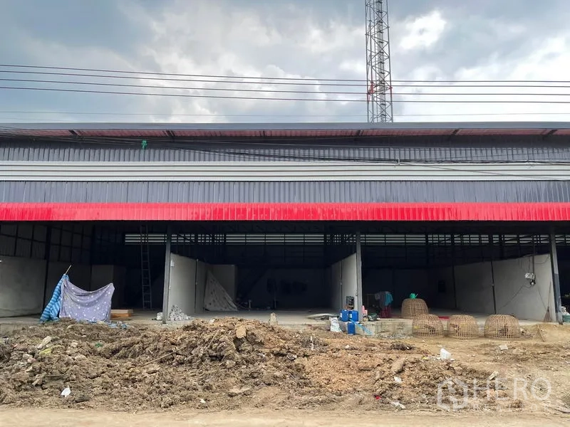货栈 出租在Pathum Thani - 红灰金属板外立面的仓库，正面开口宽阔，前方为施工土地。