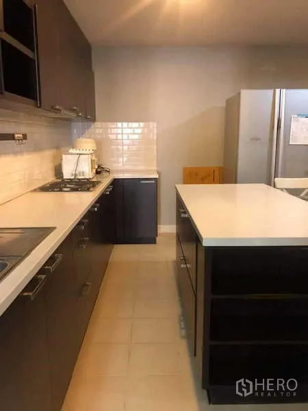 公寓 出售在Yan Nawa, Bangkok - 走廊式厨房，深色橱柜、白色台面中岛和燃气灶。