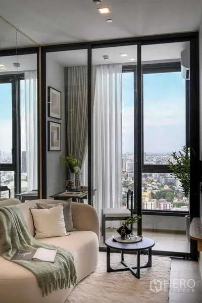 คอนโด ให้เช่าในChatuchak, Bangkok - โซฟาติดหน้าต่างสูง ผ้าม่าน และต้นไม้ในกระถาง มองเห็นเส้นขอบฟ้า