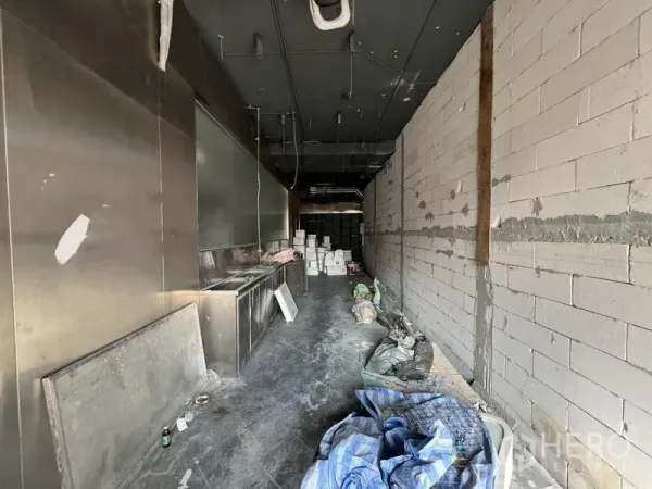 零售空间 出租 - 狭长的店铺内部，未完工，带不锈钢操作台、砌块墙和地面施工材料