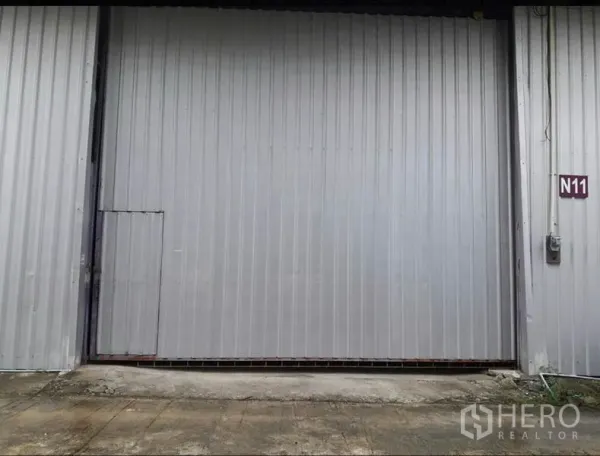 货栈 出租在Lam Luk Ka, Pathum Thani - 灰色钢制推拉仓库门特写，带侧门与N11单元标识