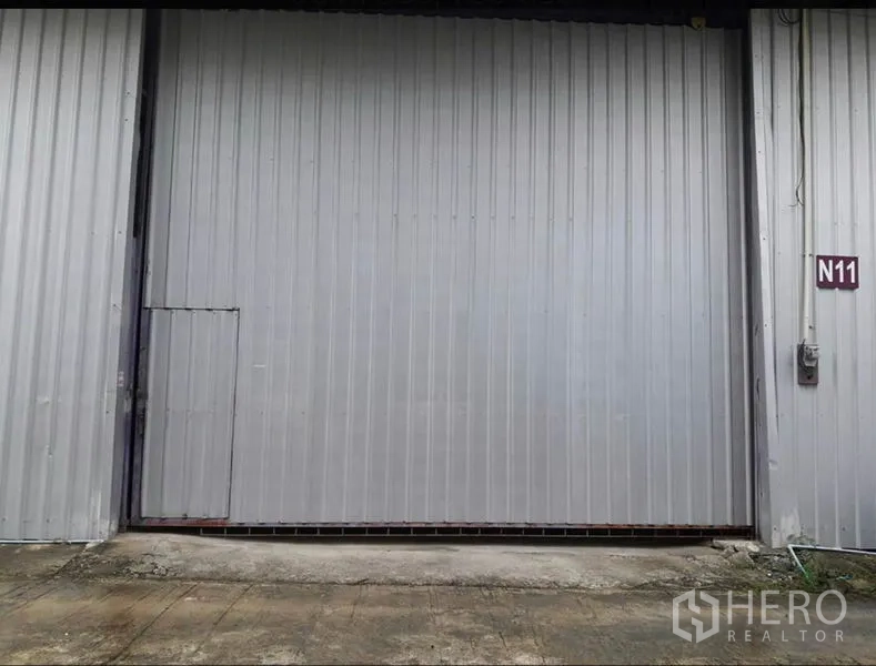 货栈 出租在Lam Luk Ka, Pathum Thani - 灰色钢制推拉仓库门特写，带侧门与N11单元标识