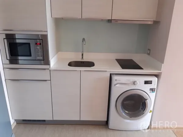 Condominium for rent or sale in Watthana, Bangkok - Compact modern kitchenette with sink, induction hob, built-in microwave and washing machine.