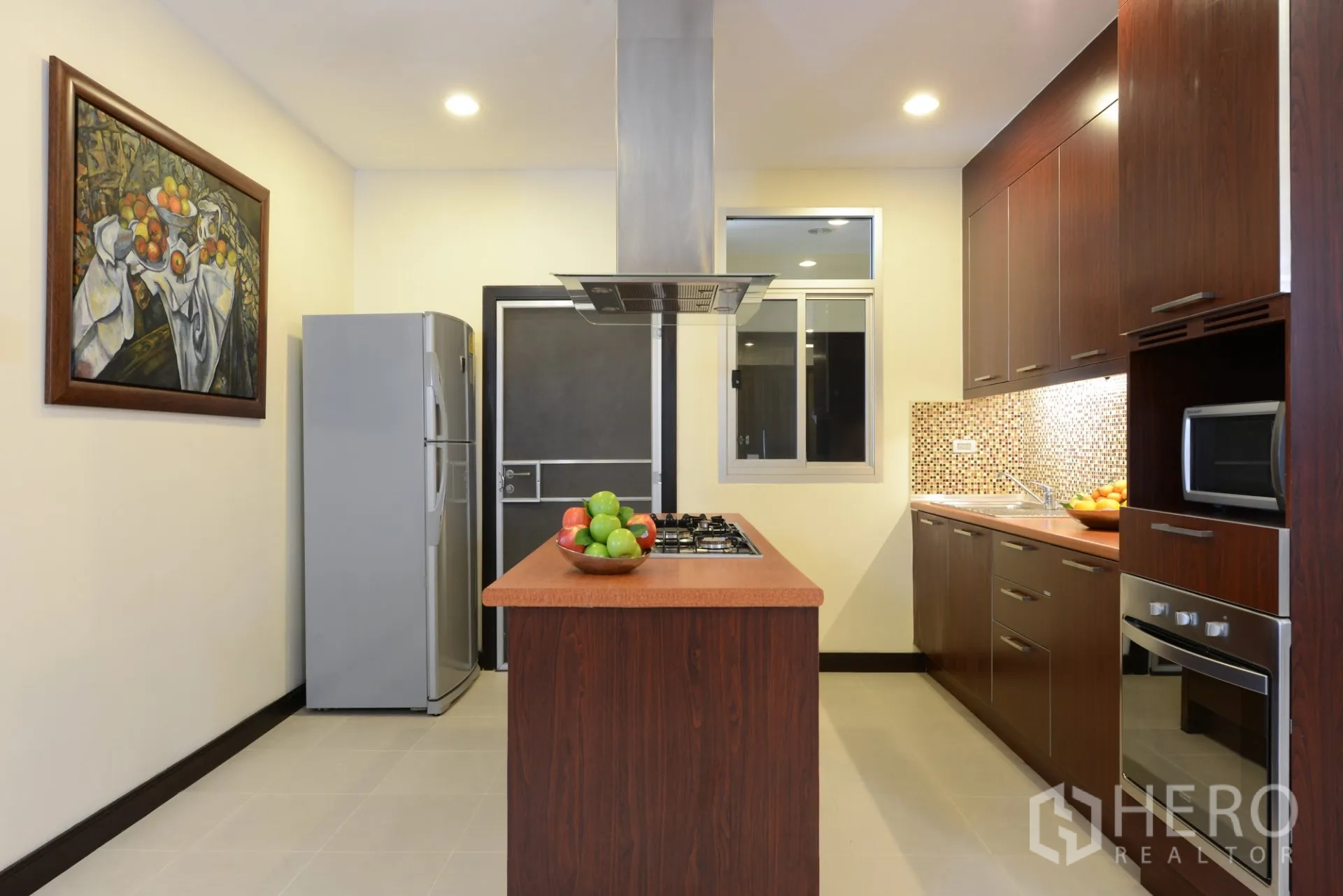 Apartment for rent in Watthana, Bangkok - Contemporary kitchen with island cooktop, stainless range hood, fridge, and ample cabinetry.