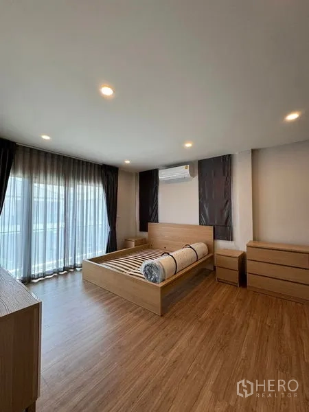 Detached House for rent in Don Mueang, Bangkok - Master bedroom with wooden flooring, large windows, air conditioner and balcony-facing curtains.