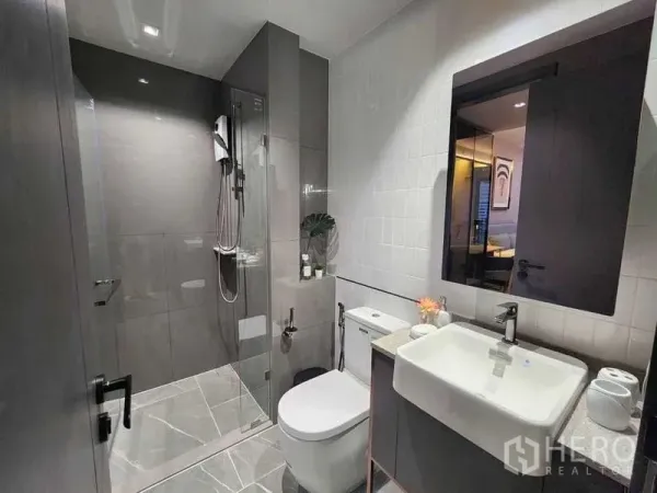 Condominium for rent in Bang Rak, Bangkok - Stylish bathroom with glass shower enclosure, vanity and large wall mirror.