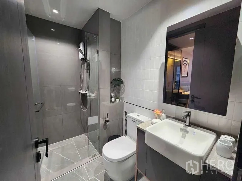 Condominium for rent in Bang Rak, Bangkok - Stylish bathroom with glass shower enclosure, vanity and large wall mirror.