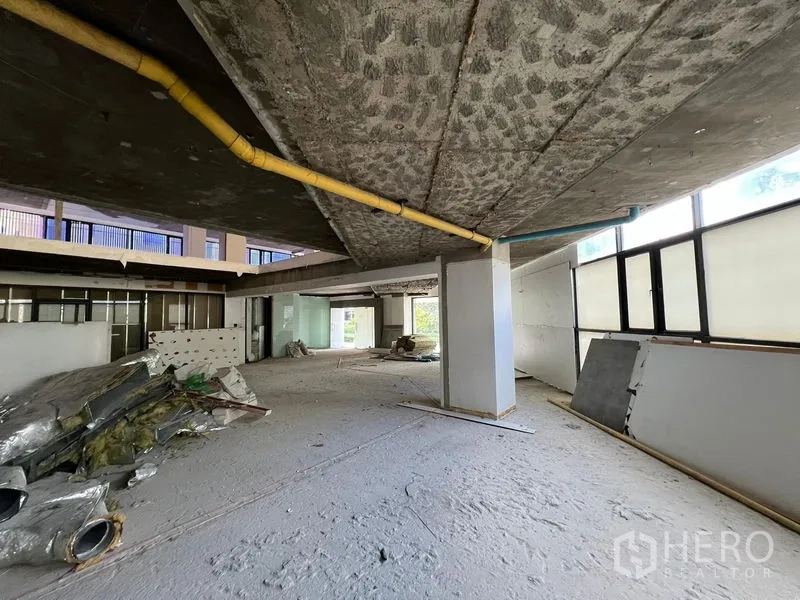 零售空间 出租在Watthana, Bangkok - 开放式毛坯空间，外露管线与大窗，地面有施工材料。