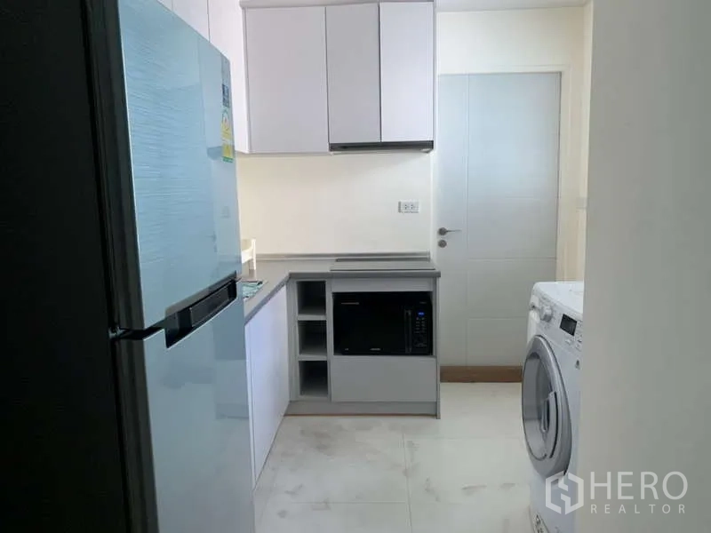 Condominium for rent in Khlong Toei, Bangkok - Secondary pantry with white cabinets, refrigerator, microwave and washing machine.