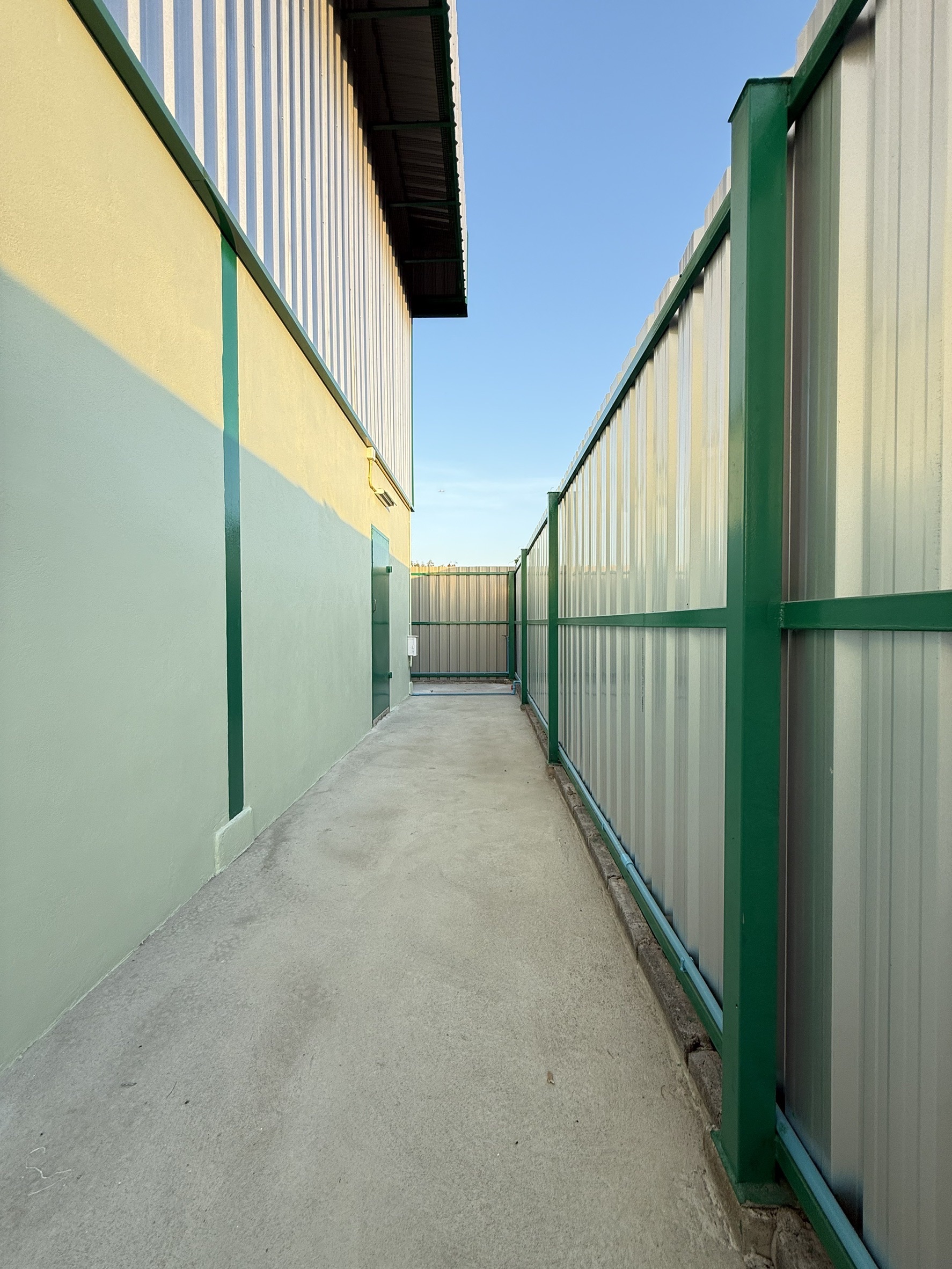 Warehouse for rent in Lat Krabang, Bangkok - Gated side passage around the building with concrete walkway and metal fence.