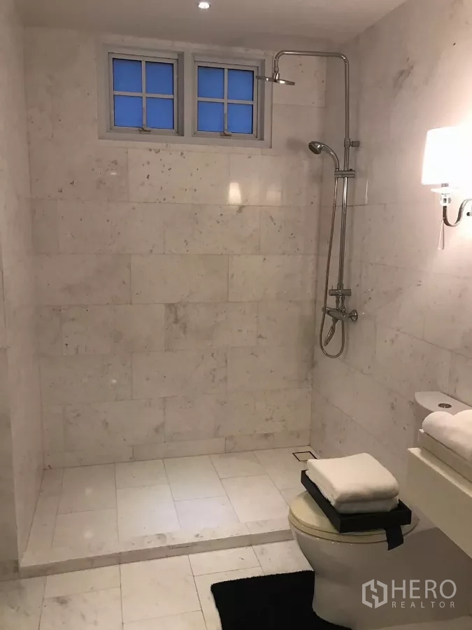Townhouse for sale in Watthana, Bangkok - Marble bathroom with walk-in shower, toilet and small frosted window.
