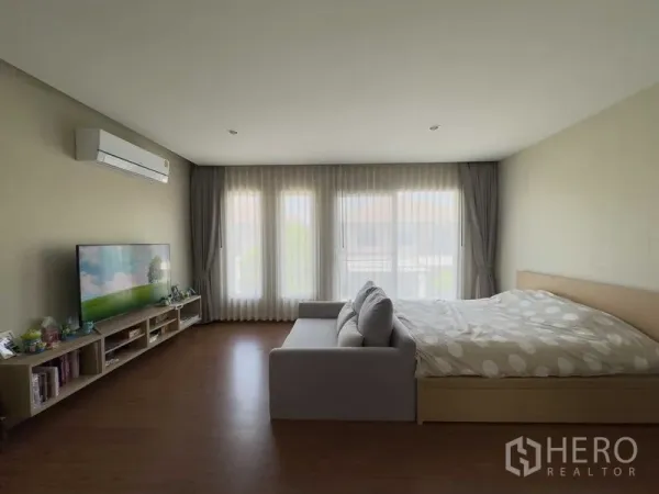 บ้าน ให้เช่าหรือขายในBang Khen, Bangkok - ห้องนอนมาสเตอร์กว้าง ผนังกระจกเต็มบาน โซฟา ทีวี และพื้นลายไม้