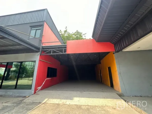 零售空间 出租在Saphan Sung, Bangkok - 带顶棚的车道入口连接两侧建筑，红黄墙面与侧窗。