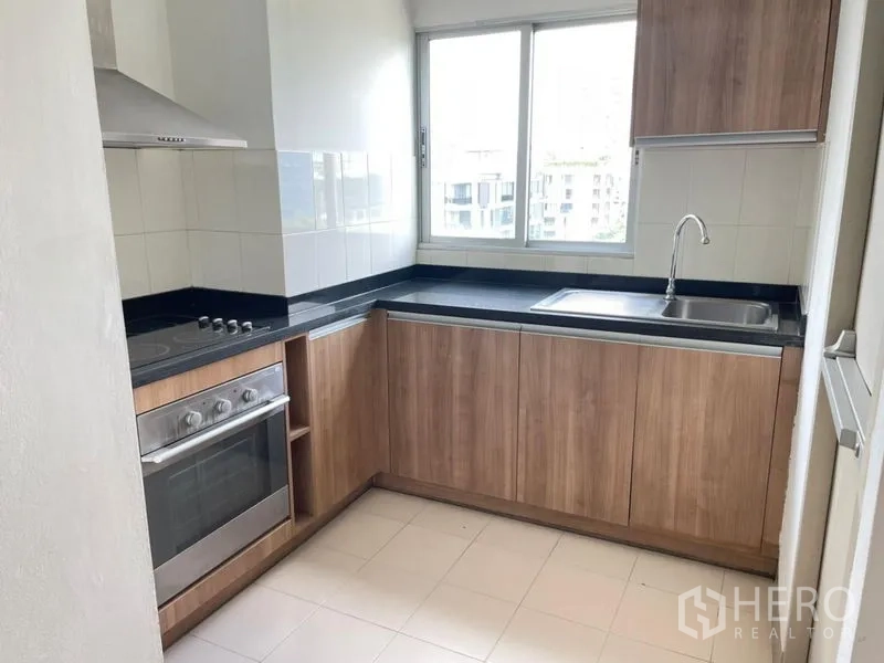 คอนโด ให้เช่าในKhlong Toei, Bangkok - ครัวรูปตัว U มีหน้าต่าง ตู้ไม้ เตาไฟฟ้า เตาอบ และท็อปหินสีดำ