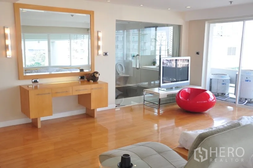 คอนโด ให้เช่าในKhlong Toei, Bangkok - ห้องนั่งเล่นสว่างพื้นไม้ มีโต๊ะเครื่องแป้งลอย กระจกบานใหญ่ ห้องน้ำผนังกระจก ทีวี และทางออกระเบียง