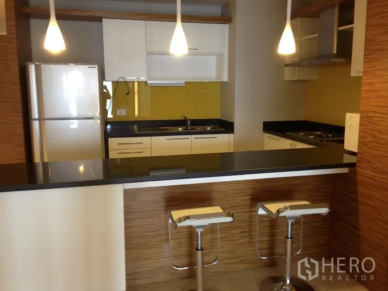Condominium for rent in Khlong Toei, Bangkok - Modern kitchen with black stone countertop, breakfast bar, pendant lights and full-size fridge.