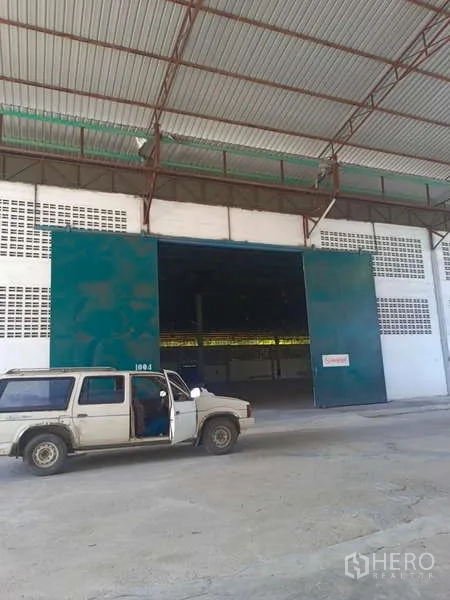 货栈 出租在Mueang Rayong, Rayong - 仓库入口配宽滑门，外有车辆停放。