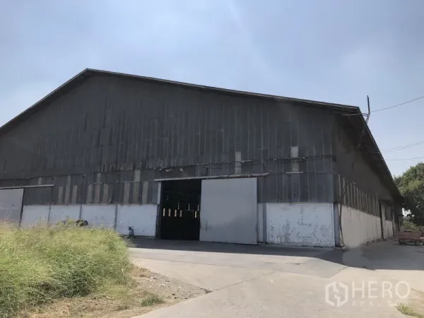 Warehouse for rent in Nonthaburi - Front elevation of an industrial warehouse with multiple sliding doors and open yard.