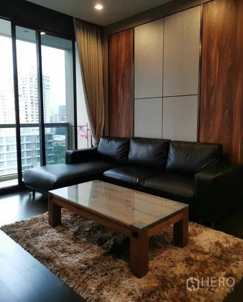 公寓 出租或出售在Watthana, Bangkok - 客厅配黑色皮沙发、玻璃茶几，连接阳台欣赏城市景观。