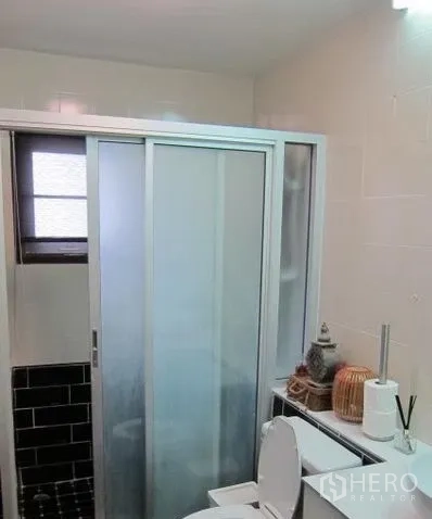 Townhouse for rent in Khlong Toei, Bangkok - Bathroom with sliding glass shower enclosure, toilet and small window.