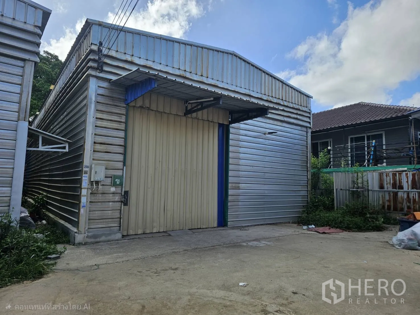 Warehouse for rent in Bang Phli, Samut Prakan - Exterior of a metal-clad warehouse with a large sliding shutter gate and small front yard.