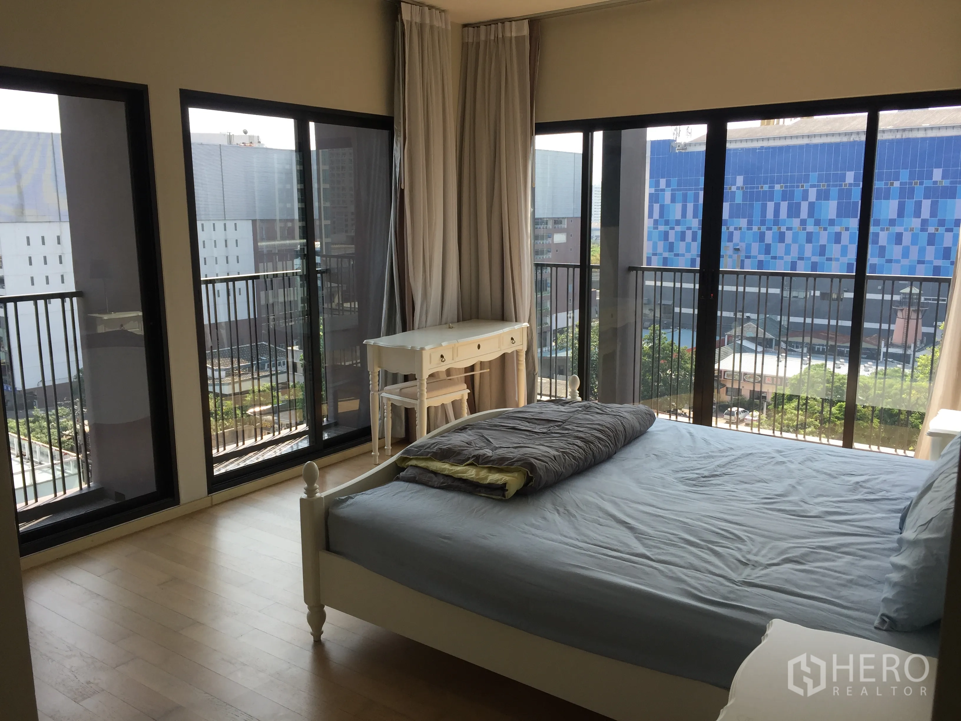 Condominium for rent or sale in Watthana, Bangkok - Corner bedroom wrapped in floor‑to‑ceiling windows showcasing urban skyline views near BTS Ekkamai.
