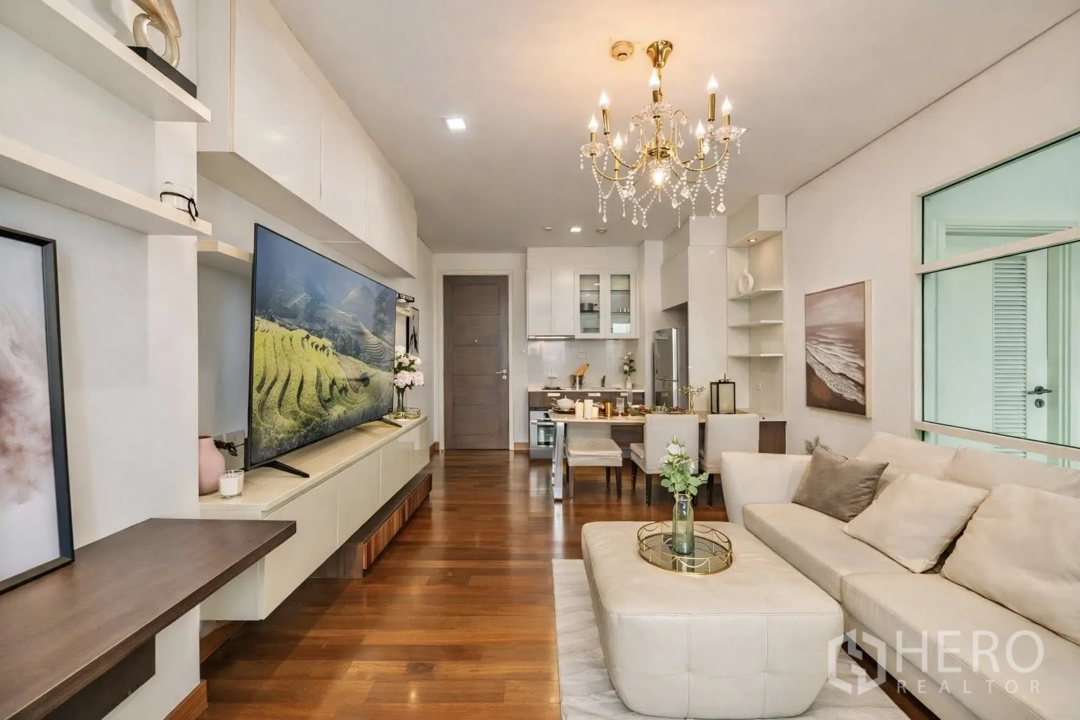 Condominium for rent or sale in Watthana, Bangkok - Open-plan living room with chandelier, sofa, and TV leading to kitchen and dining.