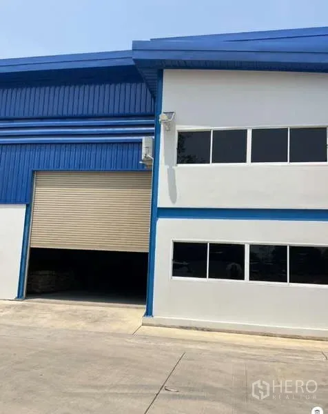 Warehouse for rent in Bang Bua Thong, Nonthaburi - Blue-and-white warehouse exterior with office windows and a wide roller shutter entrance.
