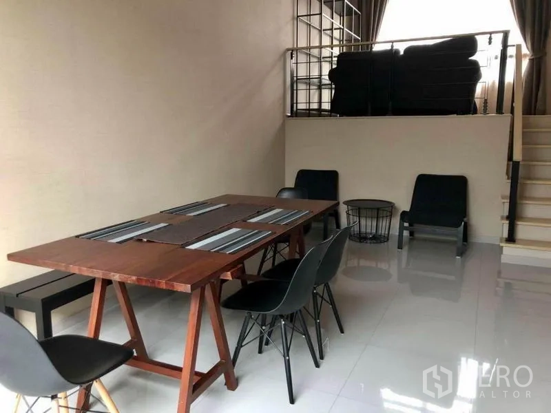 Townhouse for rent in Suan Luang, Bangkok - Dining area with wooden table and black chairs on glossy tiles below the mezzanine.