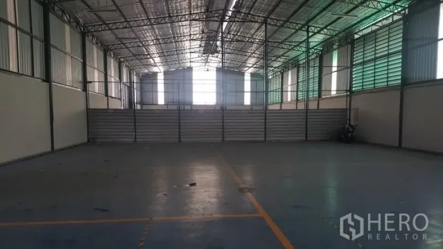 Warehouse for rent in Suan Luang, Bangkok - Spacious high-clearance warehouse with steel truss roof, translucent wall panels and marked concrete floor.