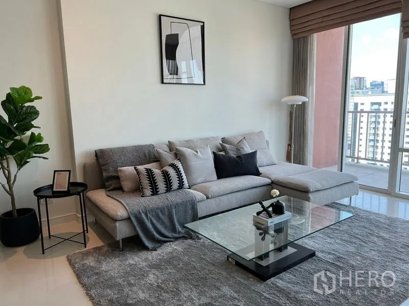 公寓 出租在Watthana, Bangkok - 起居角落，灰色L形沙发、玻璃茶几、大地毯，连通阳台。