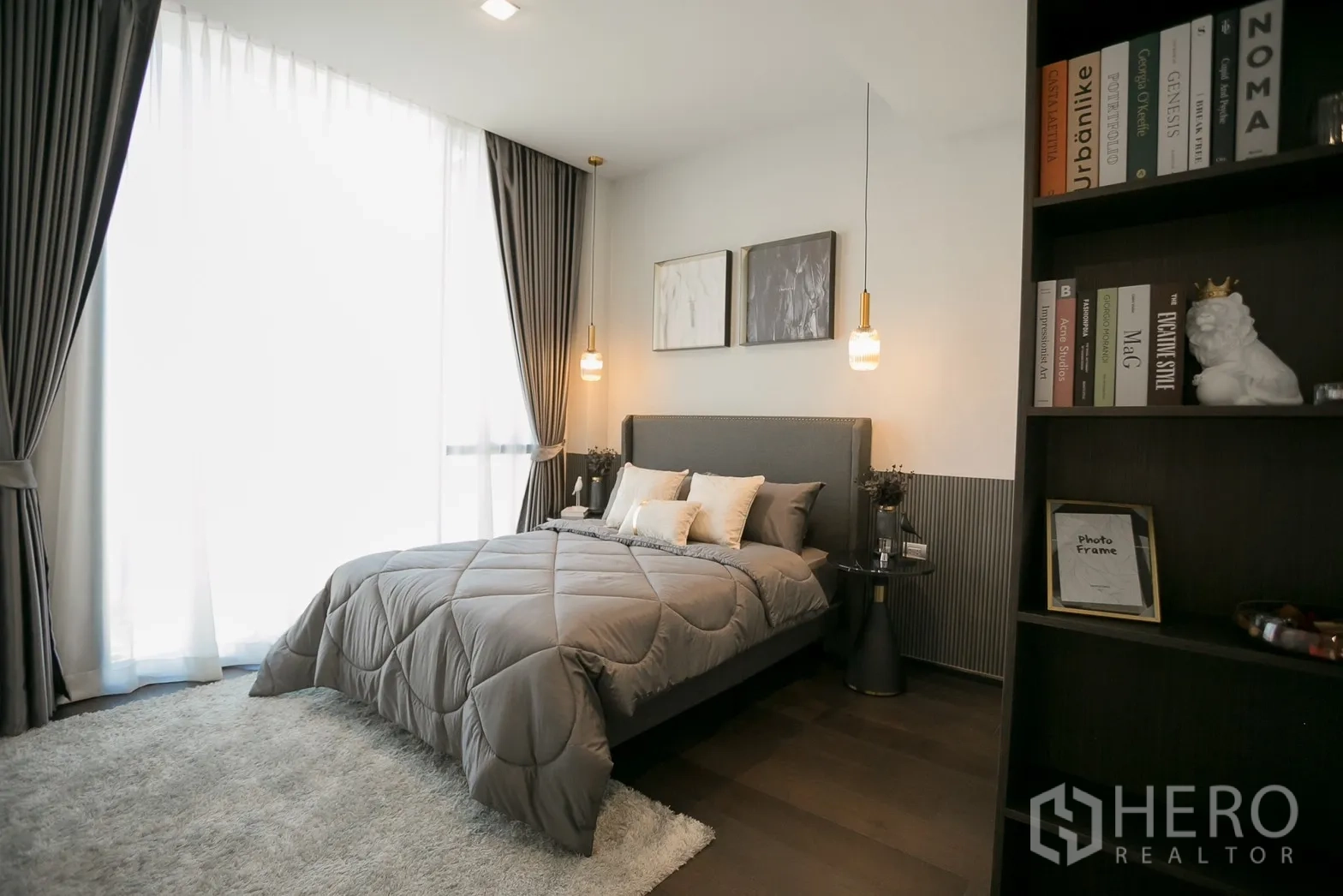 Condominium for rent in Watthana, Bangkok - Modern bedroom with grey bedding, pendant lights, floor-to-ceiling curtains, dark wood flooring, and a built-in bookshelf.