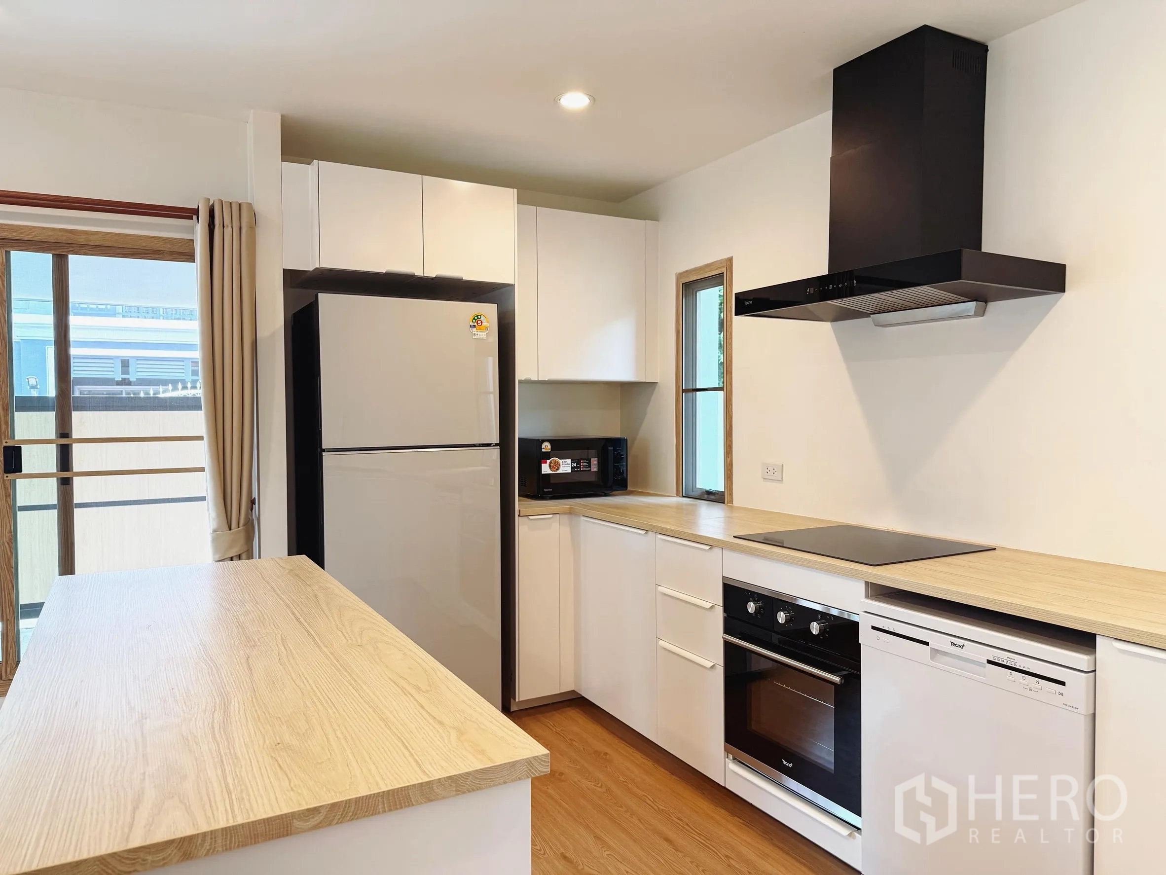 独立式住宅 出售在Suan Luang, Bangkok - 现代厨房，带中岛、嵌入式烤箱、灶台、油烟机与大冰箱。