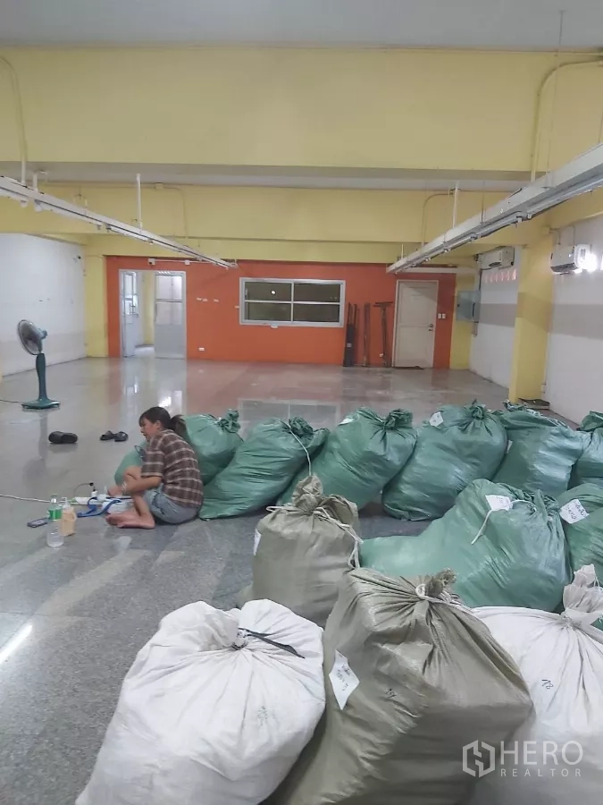 Warehouse for rent in Krathum Baen, Samut Sakhon - Spacious warehouse bay with yellow beams and rows of green sacks on the floor.