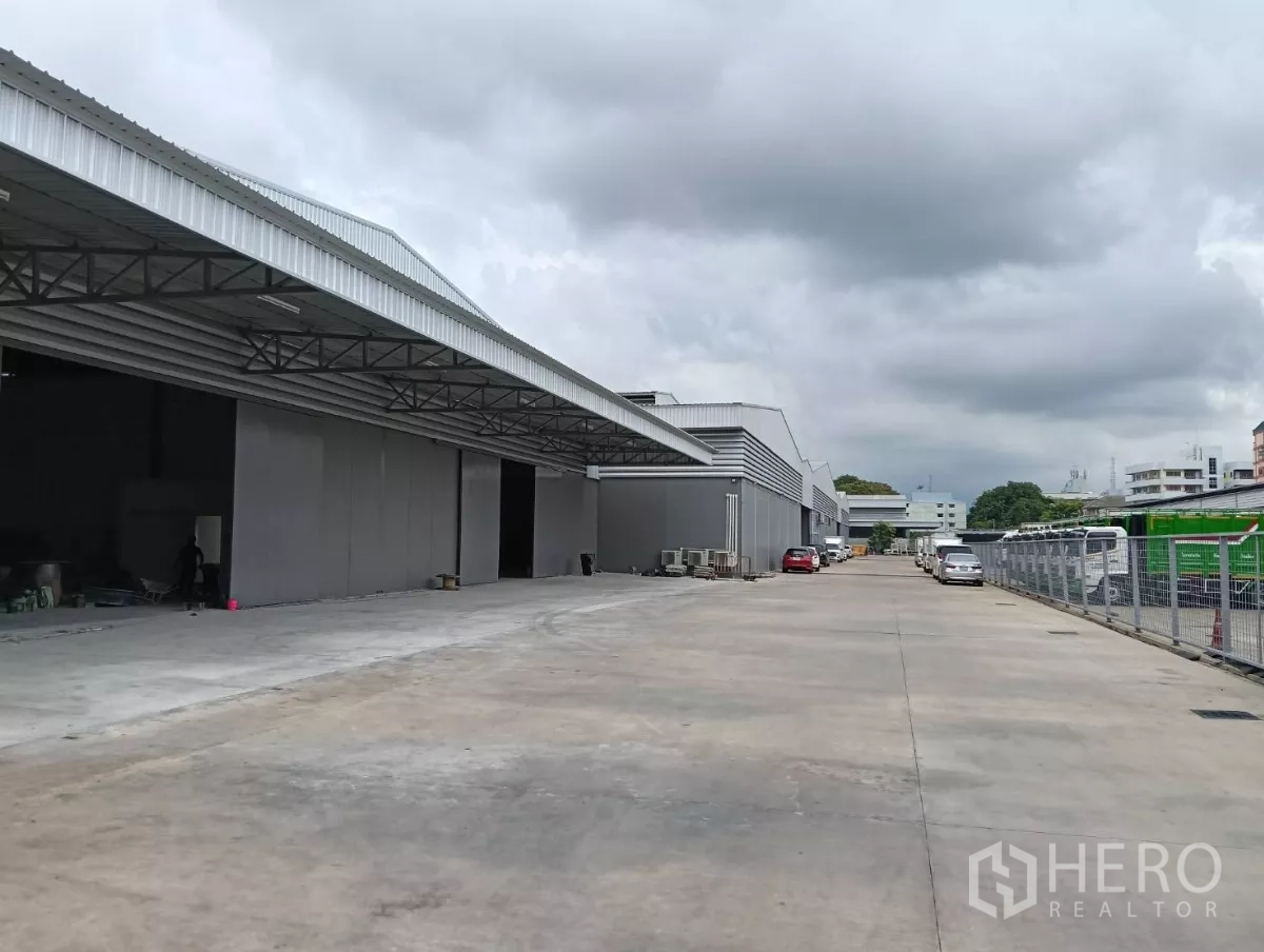 Warehouse for rent in Samut Prakan - Row of grey warehouses with covered canopies and a broad driveway designed for trucks.