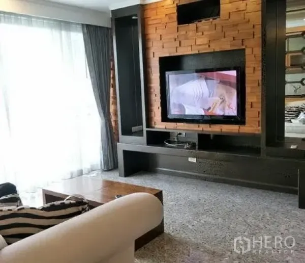 Condominium for rent or sale in Watthana, Bangkok - Bright living room with built‑in TV wall, textured wood paneling, large window and sofa.